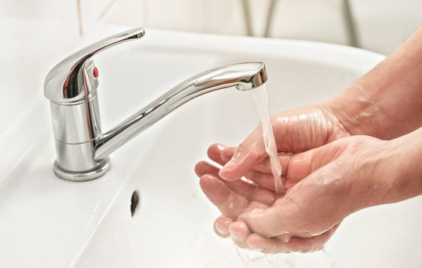 Young man washes his hands with soap under tap water faucet, closeup detail. Can be used as hygiene illustration concept during ncov coronavirus / covid 19 outbreak prevention - Photo, image
