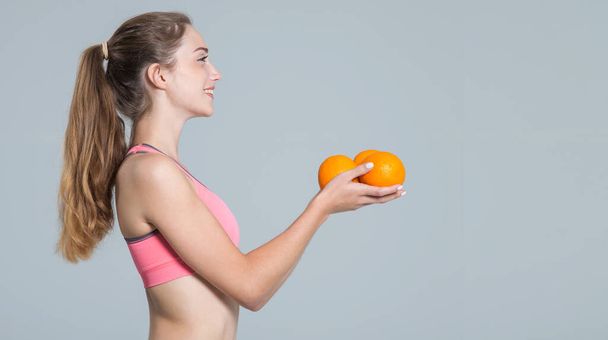 Young woman holding citrus oranges in her hands while standing on gray background. Side view. - Photo, Image