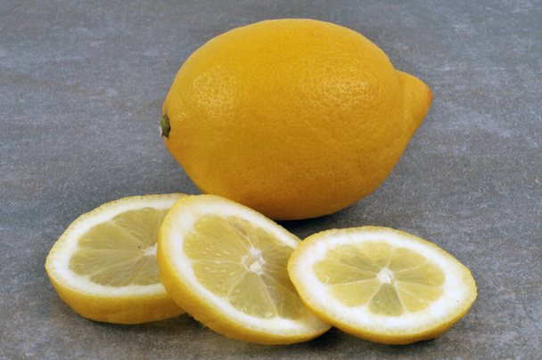 Zitronenscheiben und ganze Zitrone in Nahaufnahme auf grauem Hintergrund  - Foto, Bild