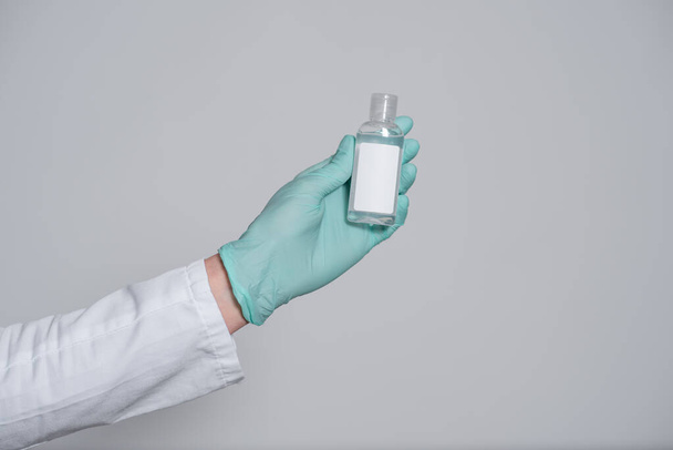 gel antiséptico para la protección contra virus infecciosos en la mano en un guante médico azul, bacterias y gérmenes sobre un fondo gris
 - Foto, Imagen