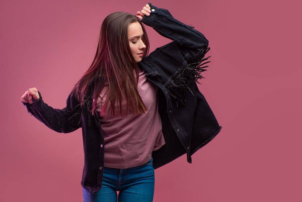 cheerful girl in a fringed jacket dances on a pink background. - Photo, image