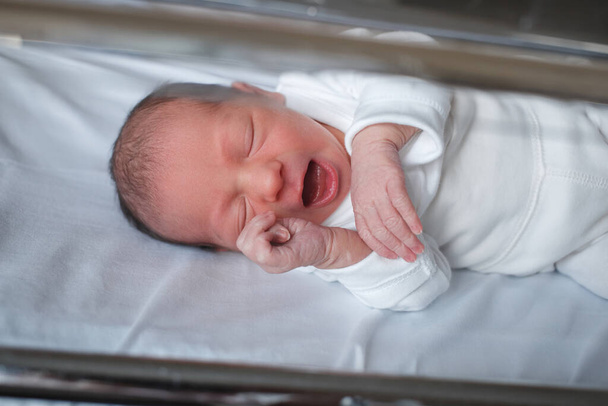 入院中の新生児。赤ちゃんが生まれたばかりです。眠そうな赤ちゃんありますザ · ベビーベッド. - 写真・画像