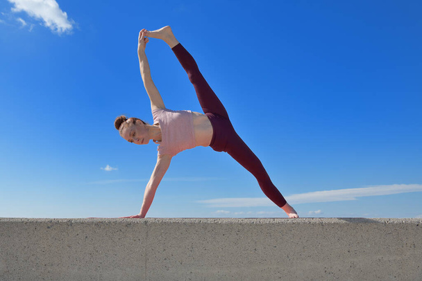 Portrait of a fit woman who practices yoga outdoors. Woman practicing asanas on a sunny day with a blue sky in the background - 写真・画像