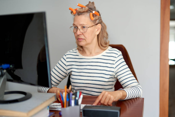 Frau mit Lockenwickler auf dem Kopf blickt auf Computerbildschirm - Foto, Bild