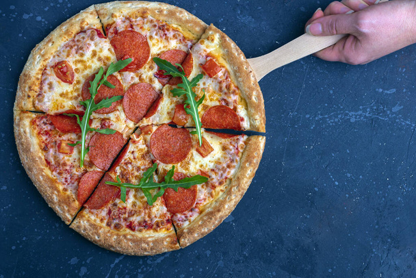 Female hand holds pizza with culinary shovel. Fresh prepared pepperoni pizza with salami and cheese on a dark background. Italian traditional lunch or dinner. Fast food and street food concept. - Photo, image