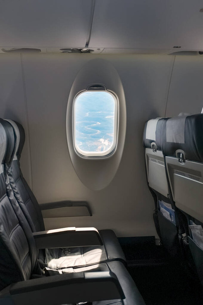 Wnętrze samolotu bez pasażerów. Widok pustego rzędu siedzeń i okien. Samolot jest bankowość więc można zobaczyć dolinę poniżej przez okno. - Zdjęcie, obraz