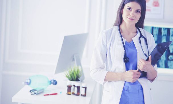 Mooie arts staande in een Consulting kamer met een map in haar handen, denken - Foto, afbeelding
