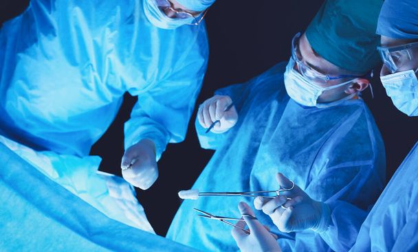 Group of surgeons at work in operating theater toned in blue. Medical team performing operation - Foto, Bild