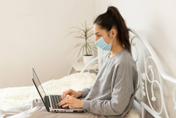 Young girl woman in protective medical mask distance learning for students. Quarantine. Freelancer, work at home, online - Φωτογραφία, εικόνα