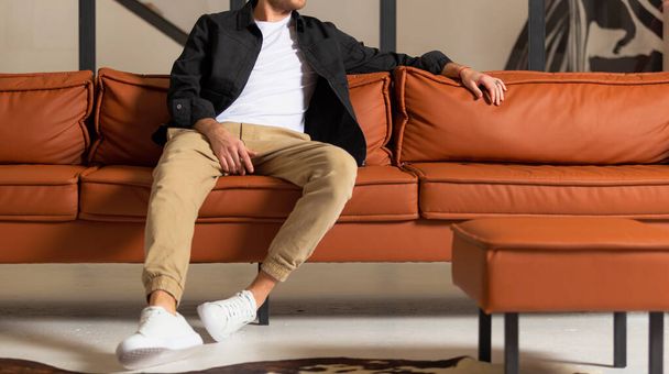 Rento komea nuori mies rentoutumassa kotona istuu sohvalla
. - Valokuva, kuva