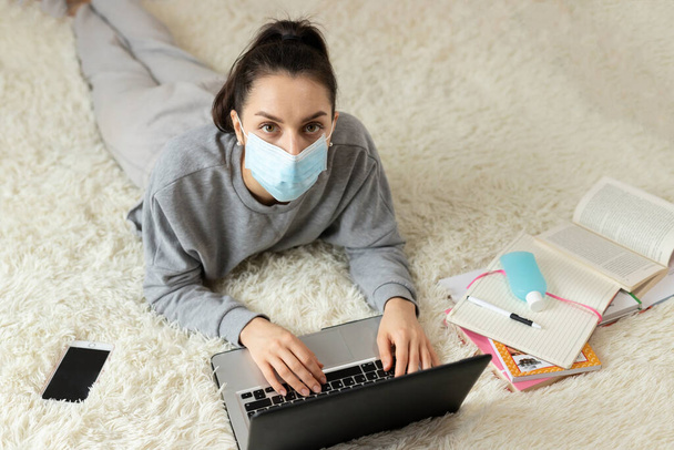 Young girl woman in protective medical mask distance learning for students. Quarantine. Freelancer, work at home, online - Fotoğraf, Görsel