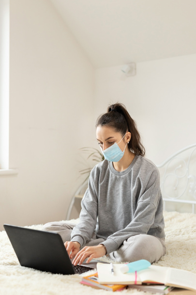 Young girl woman in protective medical mask distance learning for students. Quarantine. Freelancer, work at home, online - Fotografie, Obrázek