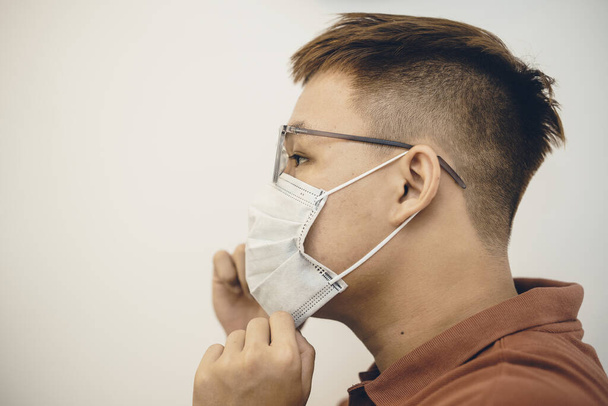 Protección contra coronavirus en el lugar de trabajo. Joven asiático hombre poniendo en mascarilla higiénica. conmocionado por el brote de 2019-nCoV o Covid 19. plano de estudio
 - Foto, Imagen