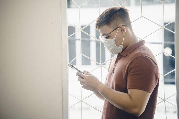Close up of one young Asian man wearing a white surgical face mask and using a mobile phone during new type Coronavirus Covid-19 pneumonia outbreak and pm 2.5 smog air pollution crisis in big city - Zdjęcie, obraz