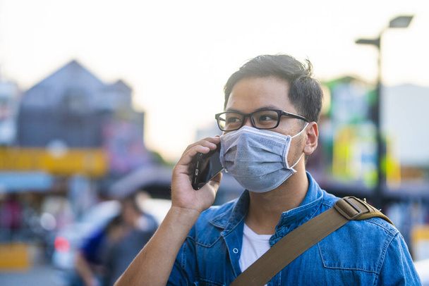 Man wearing surgical mask on street while using phone. Portrait of young man wearing a protective mask to prevent germs, toxic fumes, and dust. Prevention of bacterial infection Corona virus or Covid 19 in the air around the streets and gardens. - Foto, immagini