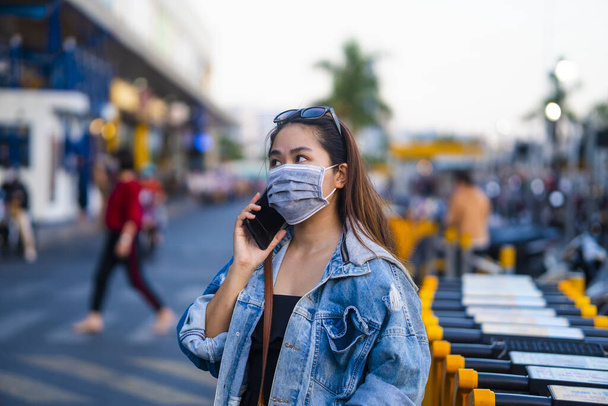 young woman wearing surgical mask on street while using mobile phone. Portrait of young woman wearing a protective mask to prevent germs, toxic fumes, and dust. Prevention of bacterial infection Corona virus or Covid 19. - Foto, Imagen