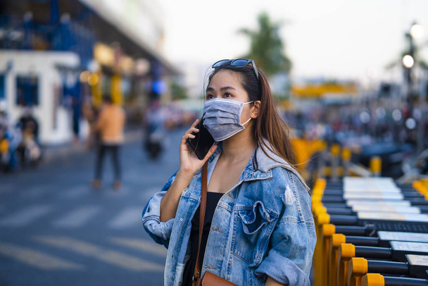 young woman wearing surgical mask on street while using mobile phone. Portrait of young woman wearing a protective mask to prevent germs, toxic fumes, and dust. Prevention of bacterial infection Corona virus or Covid 19. - Φωτογραφία, εικόνα