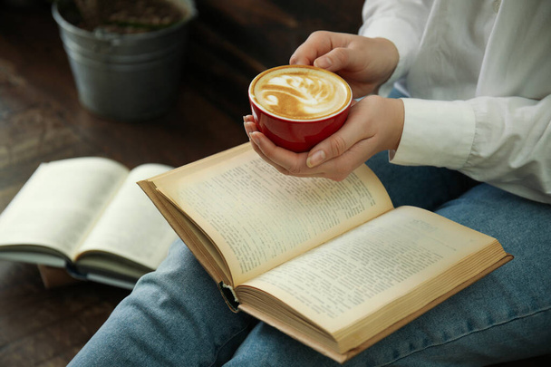 Woman with cup of coffee reading book indoors, closeup - Foto, immagini