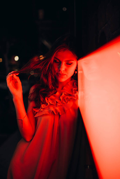 Ένα νεαρό κορίτσι με καλοκαιρινό φόρεμα κάνει βόλτες στην πόλη τη νύχτα. - Φωτογραφία, εικόνα