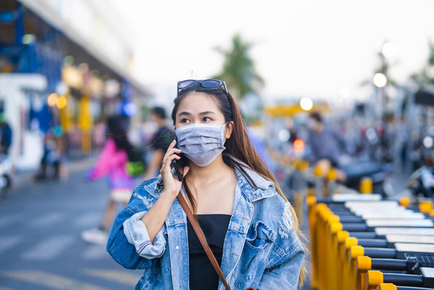 Nuori nainen yllään kirurginen naamio kadulla, kun käytät matkapuhelinta. Muotokuva nuori nainen yllään suojaava naamio estää bakteereita, myrkyllisiä höyryjä ja pölyä. Bakteeri-infektion ehkäisy Corona virus tai Covid 19
. - Valokuva, kuva