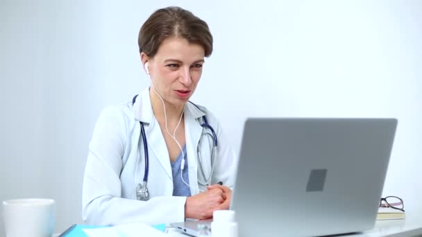 Portret van een lachende vrouwelijke arts die de patiënt adviseert door middel van videogesprekken in online chat op het computerscherm. De arts neemt contact op met de klant op de conferentie, praat op de laptops webcam. - Video