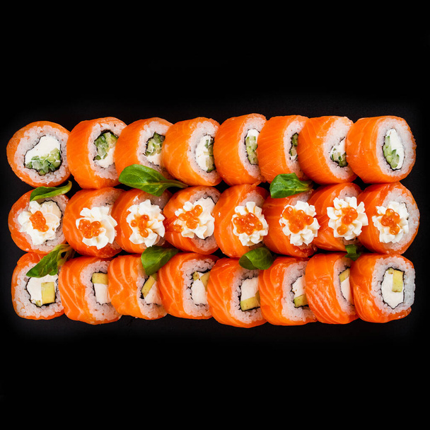 Farbige Sushi-Rollen mit Lachsfisch, Garnelen und geräuchertem Aal mit Frischkäse auf schwarzer Platte - Foto, Bild