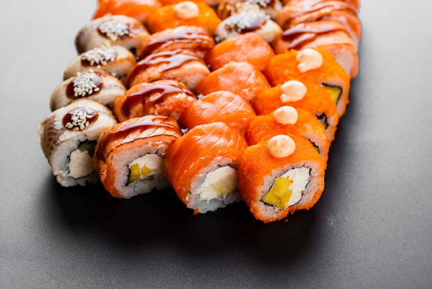 вкусные разноцветные суши с рыбой лосося, креветками и копченым угрем со сливочным сыром на черном блюде
 - Фото, изображение