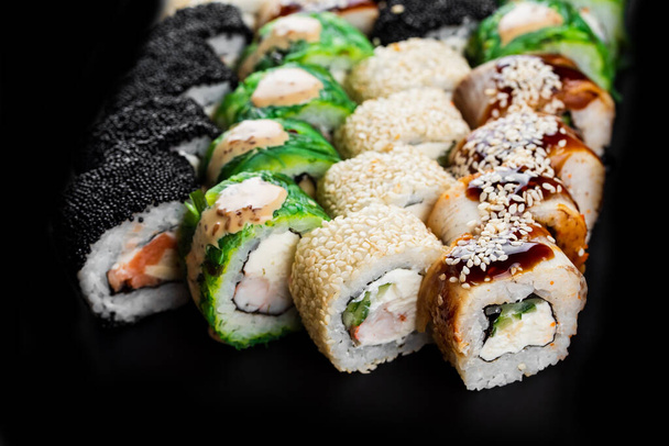 gustosi involtini di sushi colorati con pesce salmone, gamberetti e anguilla affumicata con crema di formaggio su piatto nero
 - Foto, immagini