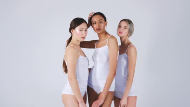 Τρία πολυεθνικά κορίτσια με τέλειο δέρμα και σώμα τύπου ποζάρουν σε λευκό πουκάμισο δεξαμενή και κιλότα σε γκρι φόντο - Πλάνα, βίντεο