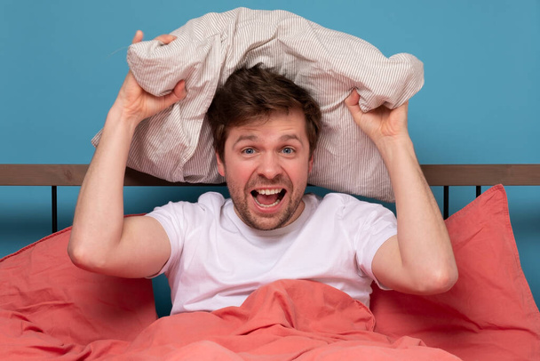 Biały mężczyzna rzucający poduszkę do łóżka. Zdjęcia studyjne - Zdjęcie, obraz