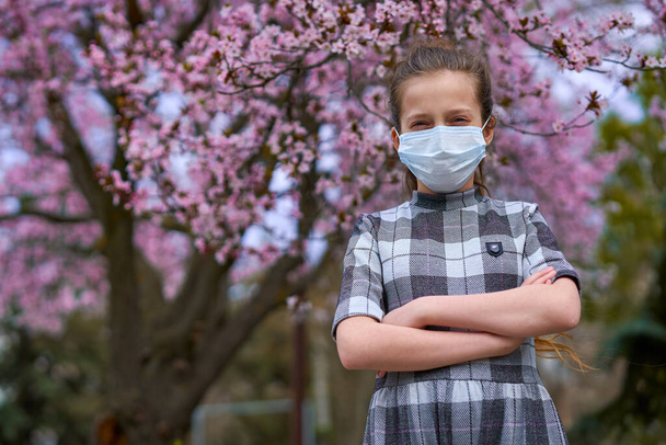 Mädchen mit Gesichtsmaske ist in der Stadt draußen, blühende Bäume, Frühlingszeit, Blütezeit - Konzept für Allergien und Gesundheitsschutz vor staubiger Luft - Foto, Bild