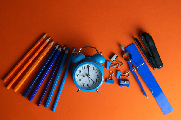 Pencils, blue alarm clock, compass, ruler and stapler on an orange background. - Foto, immagini