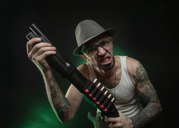 an athletic guy with a tattoo poses with a shotgun - Фото, изображение
