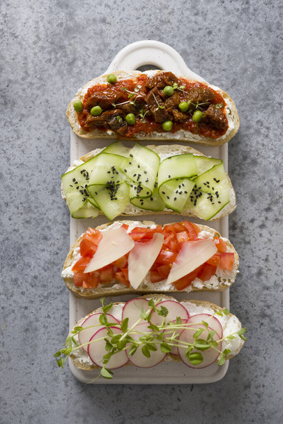 Sandwiches on toast with simple ingredients vegetables, radishes, tomatoes, cucumbers decorated microgreens on gray. View from above. Vertical format. - Φωτογραφία, εικόνα