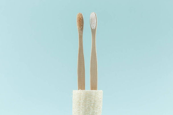 Close up of two environmentally friendly toothbrushes are in an environmental loofah. Zero waste. On a blue background. - Φωτογραφία, εικόνα