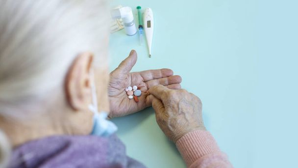 Elderly Caucasian Woman with Flu Symptoms, Home Quarantine. Holds Multicolored Pills His Hand. Concept - Dangerous Virus for Elderly, Self-Isolation. Selective Focus. Copy space. - Foto, Imagem