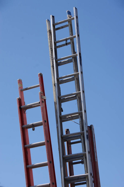 Close-up lage hoek uitzicht op de bovenste delen van verschillende opgeslagen lange hoge ladders en heldere blauwe lucht boven - Foto, afbeelding