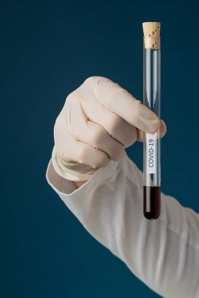 新しいCovid 19コロナウイルスの血液サンプルのテスト-血液を用いた医師保持試験管.青を背景に. - 写真・画像