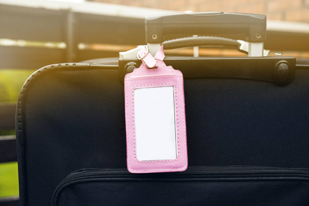 Pink feminine empty luggage tag attached to black baggage suitcase. Lost, found design element concept. - Photo, Image