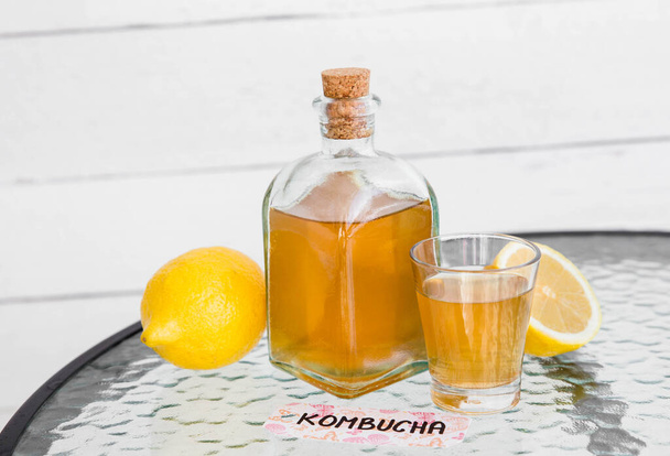 Fermented kombucha tea in a glass bottle and glass, with tag written kombucha on it, white wooden background. - Zdjęcie, obraz