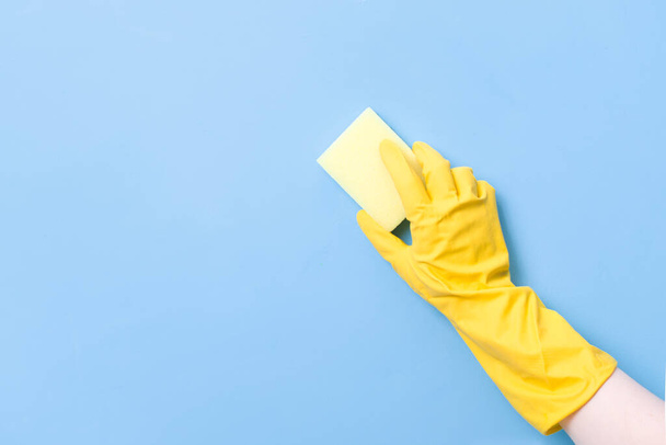 hand in a yellow rubber glove holds a yellow sponge for washing dishes and cleaning, blue background copy space, cleaning concept, household chores, spring cleaning - Фото, изображение