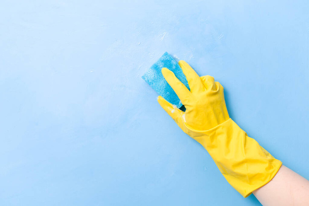 a hand in a yellow rubber glove washes a wall with a wet foamy blue sponge, foam blue background copy space, cleaning concept, household chores, spring cleaning - Фото, изображение