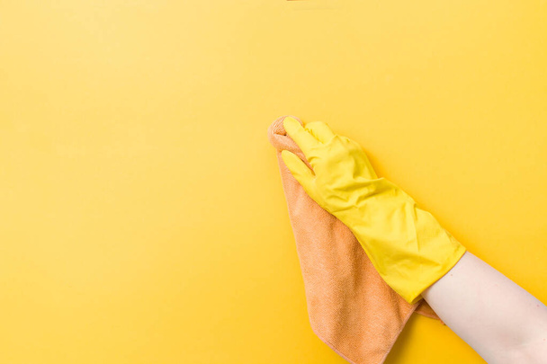 hand in a yellow rubber glove holds an orange rag for washing and cleaning, yellow background copy space, cleaning concept, household chores, wipe the dust and wash the walls - Foto, Bild