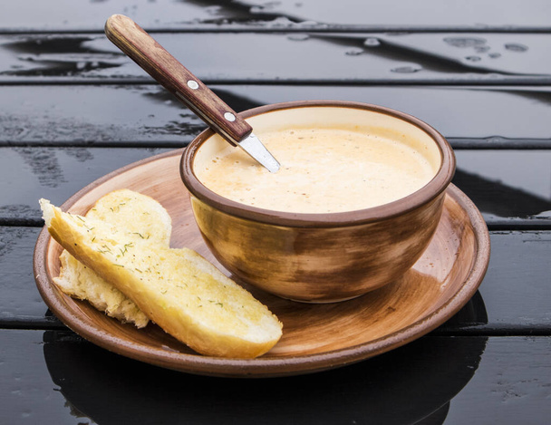 Soupe à la crème au fromage dans un bol en céramique marron et tranches de pain à l'ail sur le côté, fond en bois foncé
. - Photo, image
