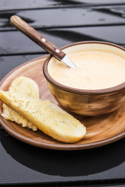 Κοντινό πλάνο ελαφριάς πορτοκαλί κρεμώδους καθαρής σούπας με τυρί και πιόνι και με φέτες ψωμιού με λάδι στο πλάι. - Φωτογραφία, εικόνα