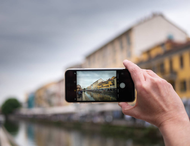 Milan, Italy  19 April 2019 - Tourist taking photo of Naviglio canal in Milan Italy with a mobile phone. Travel concept. Horizontal view - Photo, Image