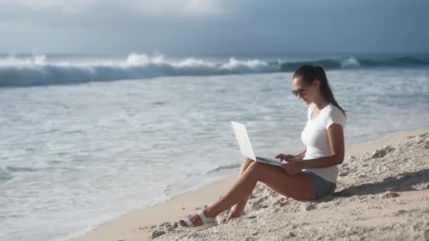 Mulher de óculos de sol trabalha na praia com laptop, abre e começa a digitar
 - Filmagem, Vídeo