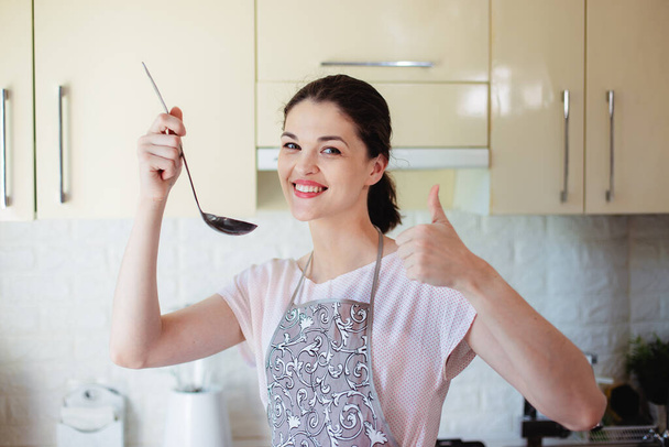 Young woman in the kitchen tastes soup on salt with a ladle. Showing thumb - Photo, Image