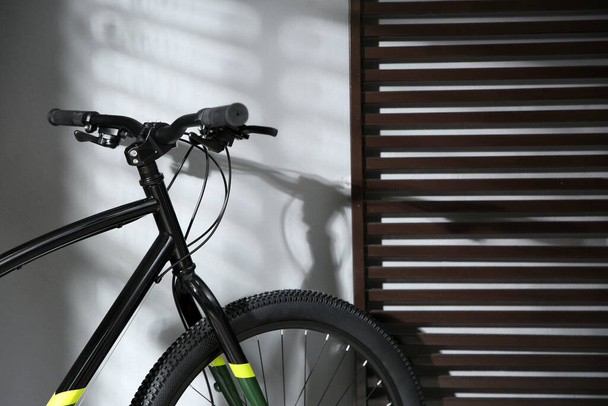 Modern black bicycle near grey wall indoors, closeup - Φωτογραφία, εικόνα