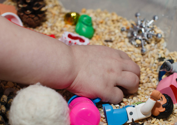 A child is looking for small figures in a sensory box. - Foto, imagen